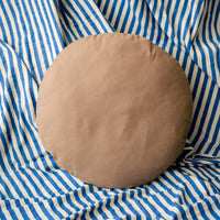 Round light brown cushion on a blue and white striped fabric background