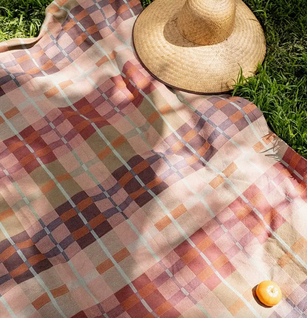 Colorful checkered blanket on grass with a straw hat and yellow ball.