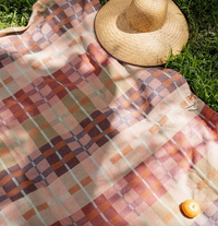 Colorful checkered blanket on grass with a straw hat and yellow ball.