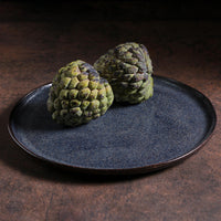 Two textured fruits on a dark plate with a dark background