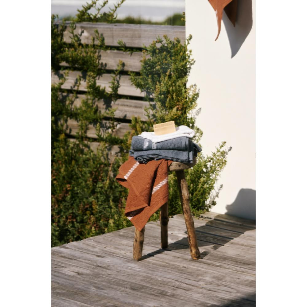 Stack of folded towels on a wooden stool outdoors with greenery in the background