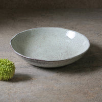 Speckled ceramic bowl on a textured surface with a green textured fruit beside it