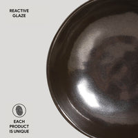 Black ceramic bowl with reactive glaze on a light gray background