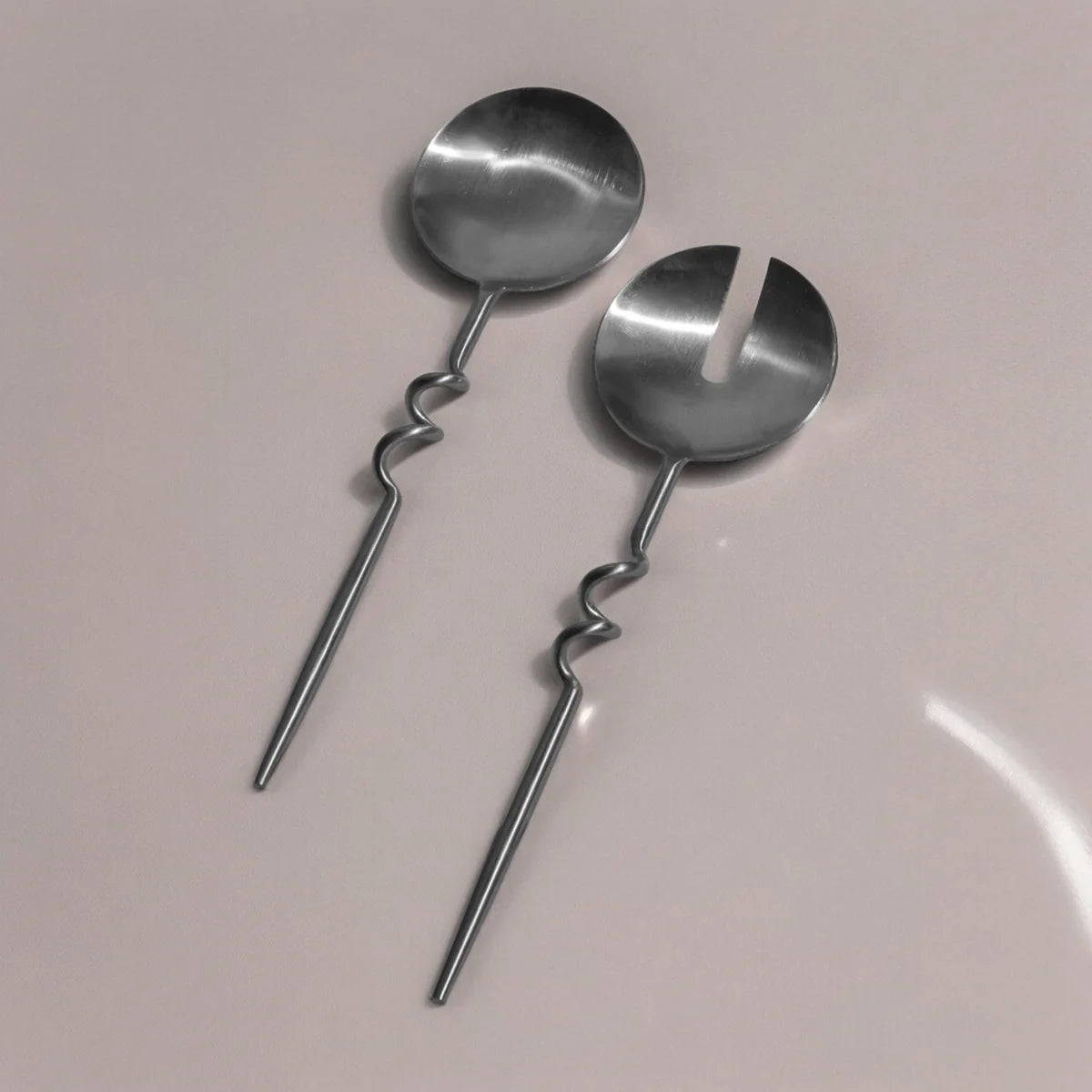Two metal serving spoons with twisted handles on a light gray background