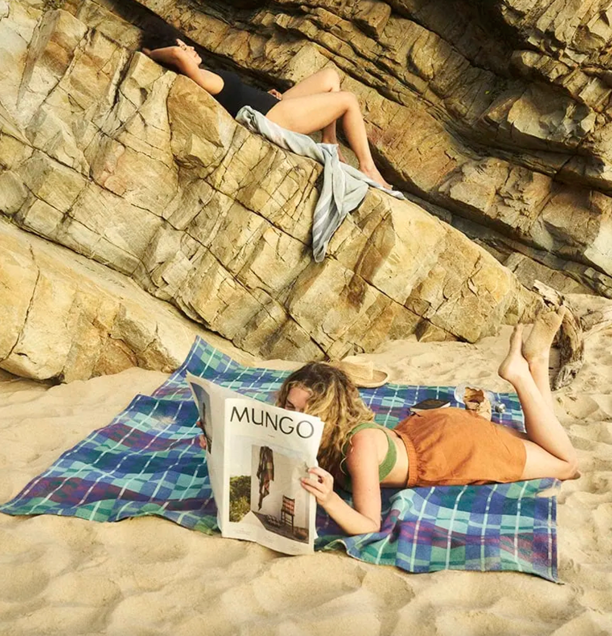 Two people relaxing on a beach with a magazine titled 'Mungo' on a colorful towel.