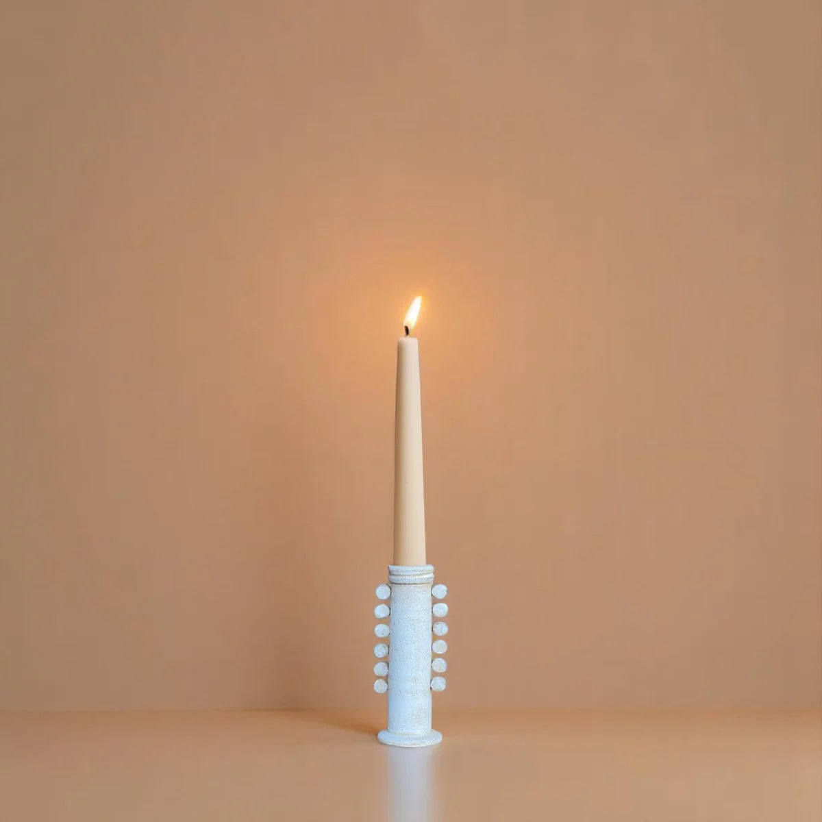 White decorative candle holder with a lit candle on a beige background