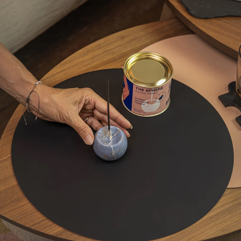Hand interacting with a small blue sphere incense holder on a black mat next to a can labeled 'The Sphere'.