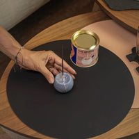 Hand interacting with a small blue sphere incense holder on a black mat next to a can labeled 'The Sphere'.