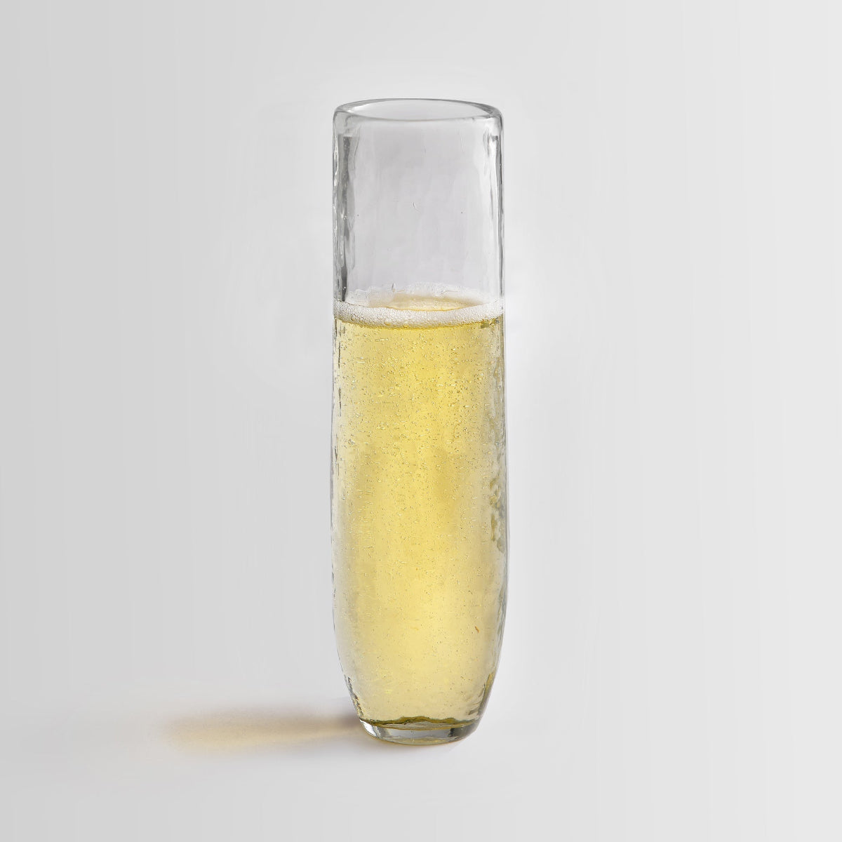 Pebbled glass stemless flute filled with champagne on a white background