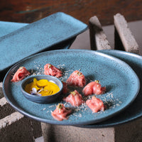 Blue ceramic plate with pink food and yellow sauce in a blue ramekin on a textured surface