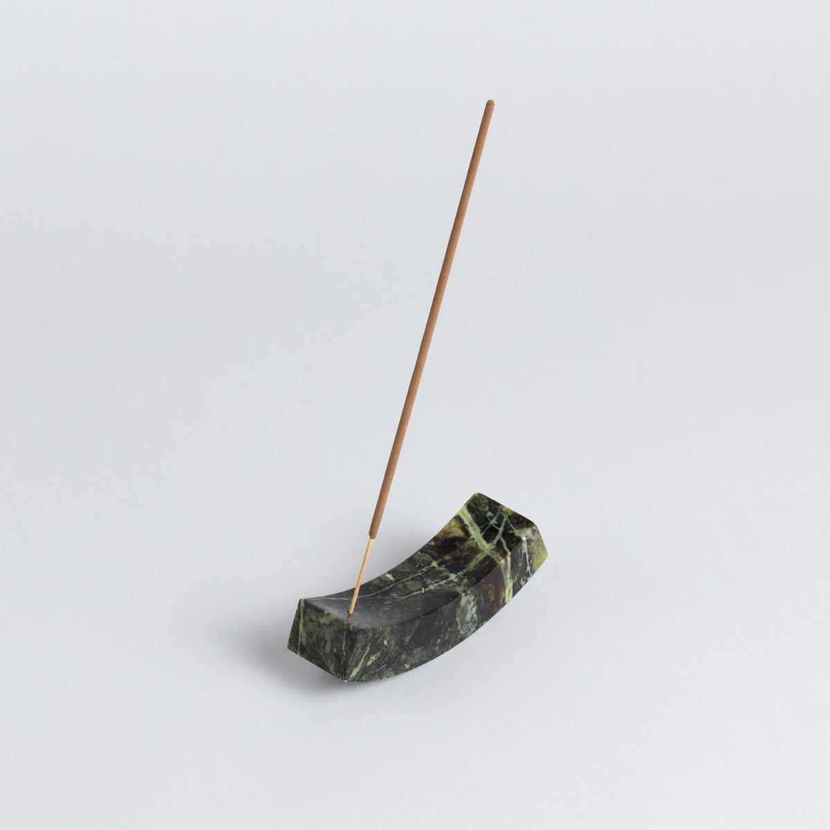 Incense stick in a green stone holder on a light gray background