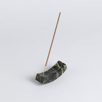 Incense stick in a green stone holder on a light gray background