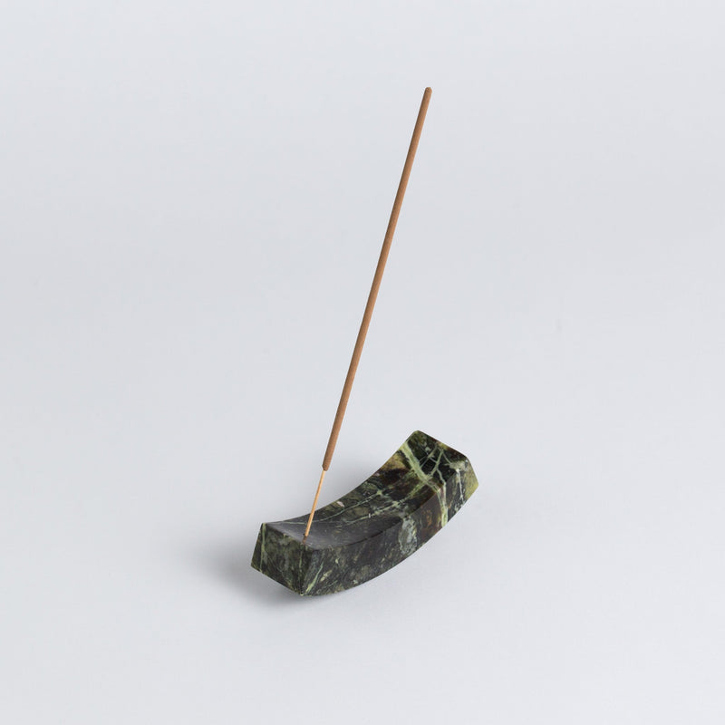 Incense stick in a green stone holder on a light gray background