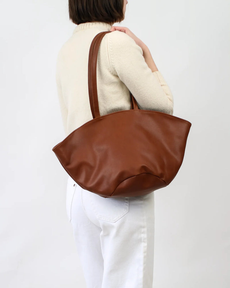 Person wearing a brown leather tote bag on a plain background