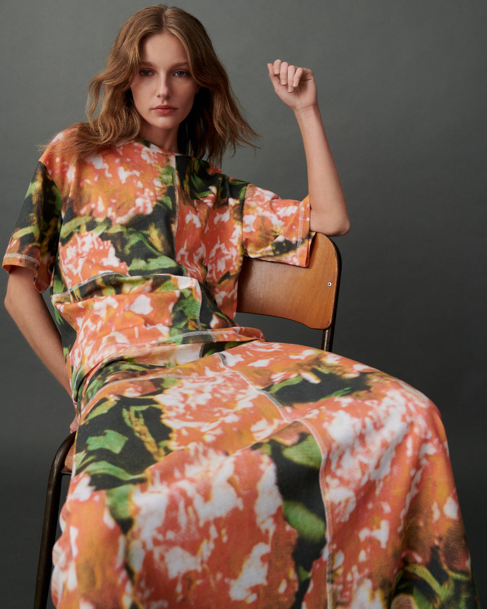 Woman wearing a floral tee and matching skirt sitting on a chair against a gray background