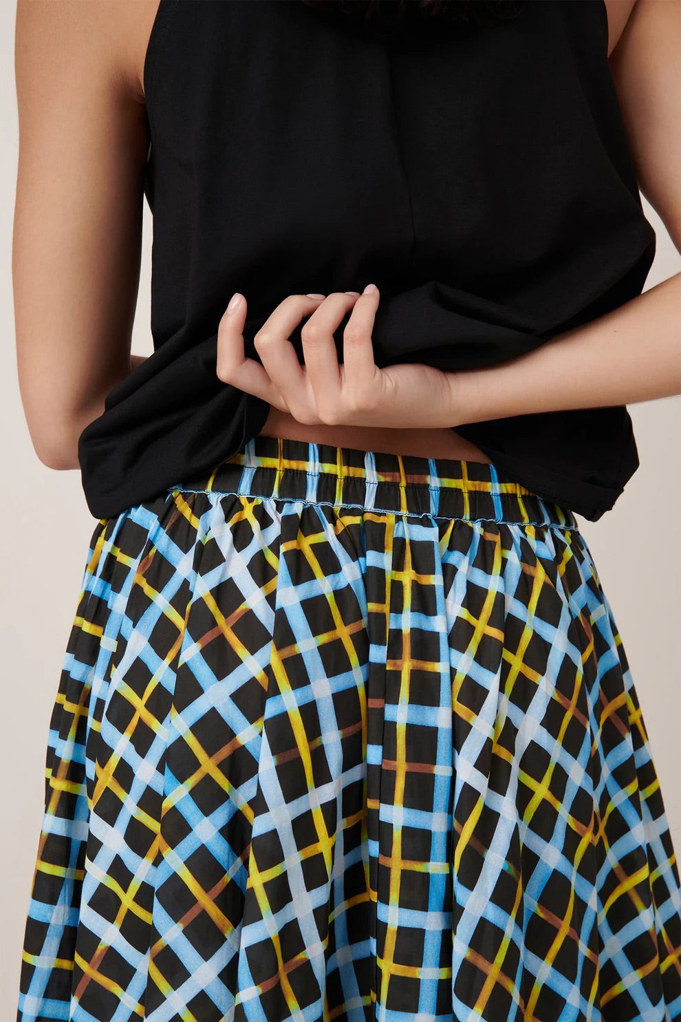 Person wearing a black top and a colorful plaid skirt on a neutral background