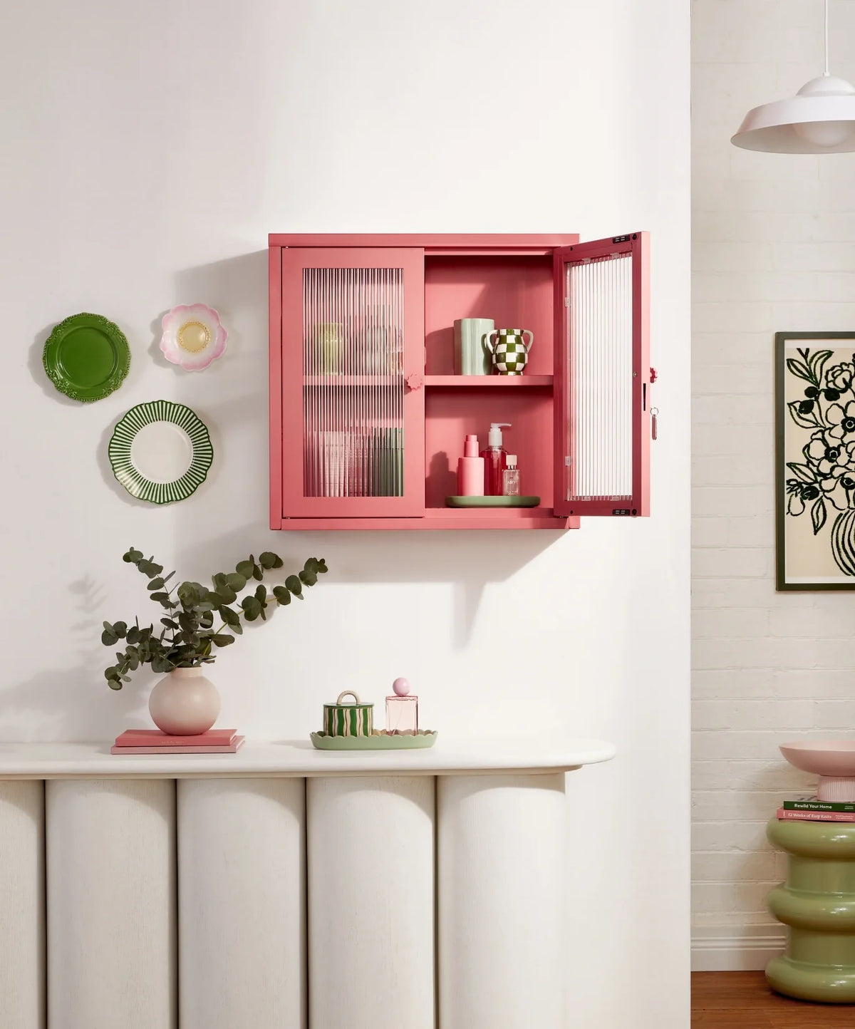 Pink wall cabinet with open door displaying items in a room with decorative elements.