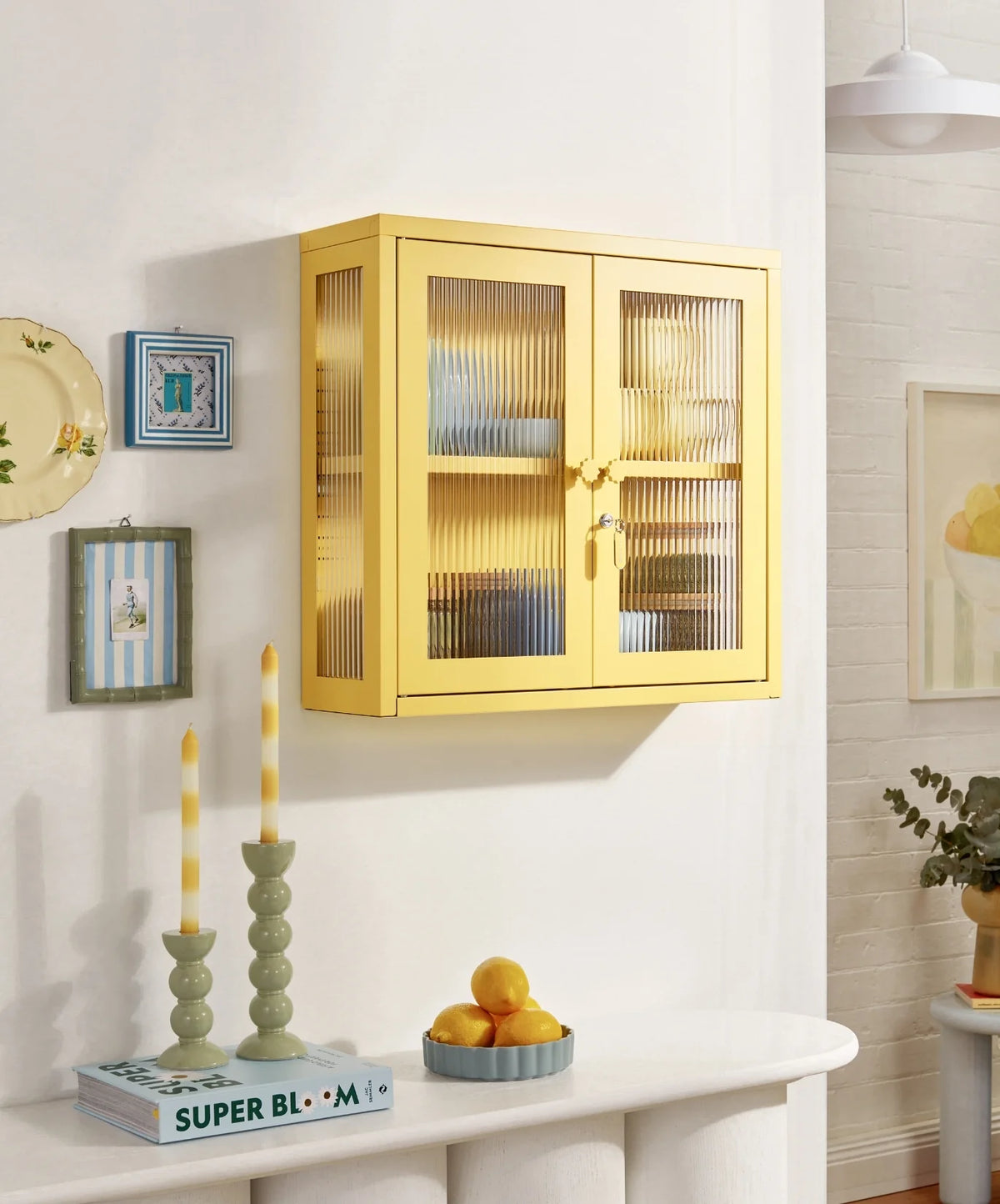 Yellow glass-front cabinet on a white wall with decorative items below.