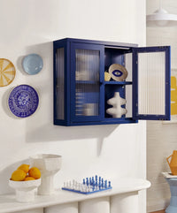 Blue cabinet with open doors displaying decorative items, plates on the wall, and a chessboard on a table.