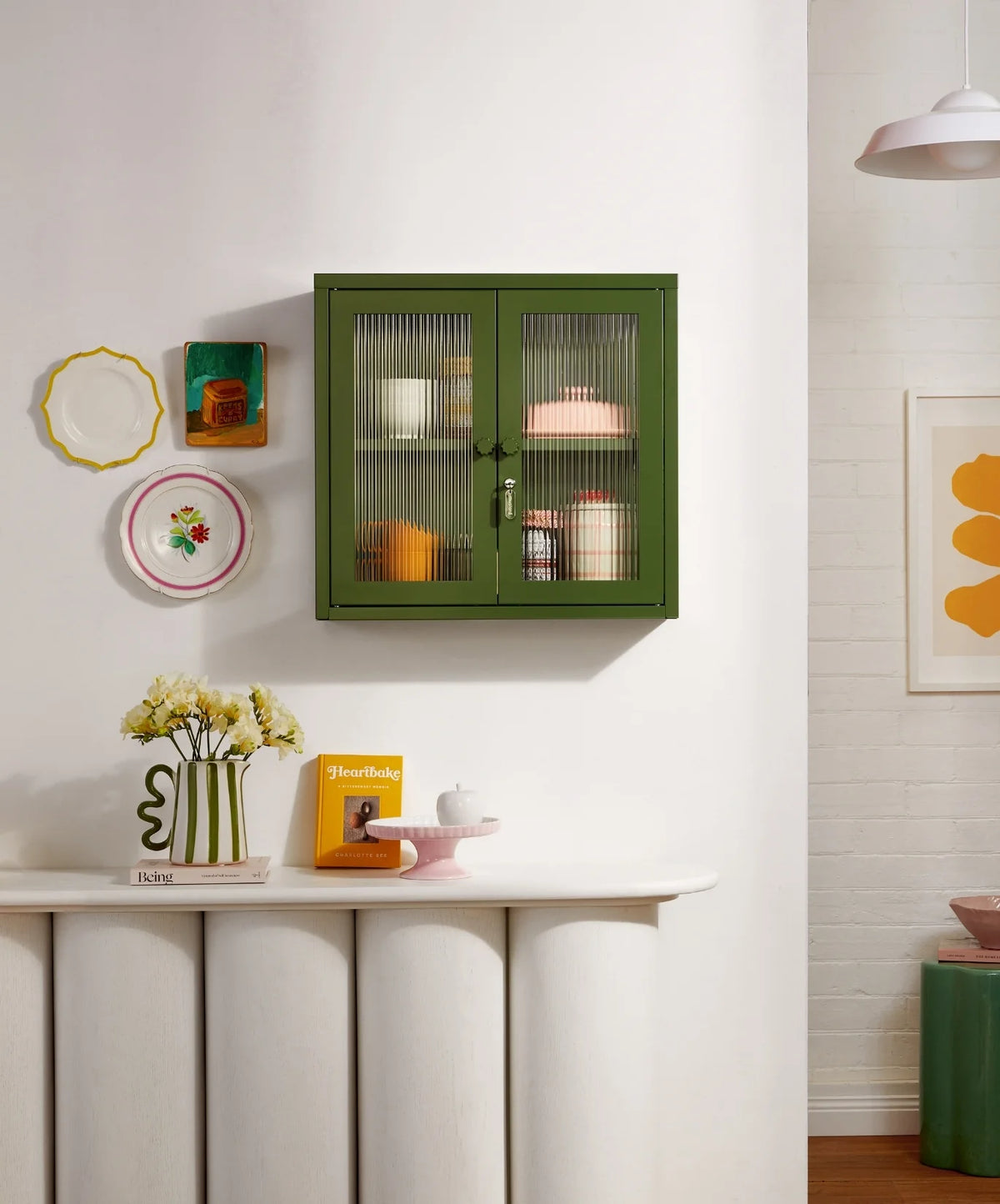 Green cabinet with glass doors in a room with decorative items on the wall and table.