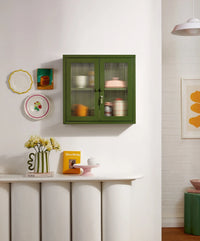 Green cabinet with glass doors in a room with decorative items on the wall and table.