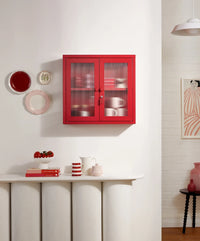 Red cabinet with glass doors in a room with decorative items on a shelf and wall.