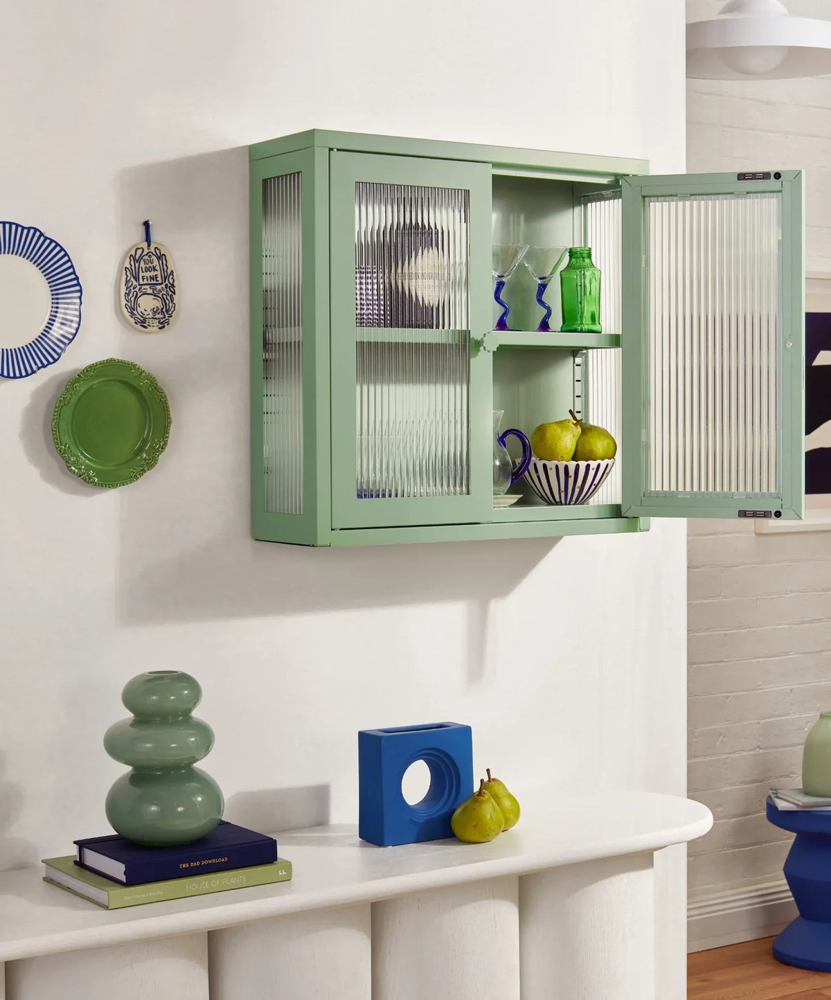 Green wall-mounted cabinet with glass doors displaying items in a room.