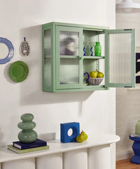 Green wall-mounted cabinet with glass doors displaying items in a room.