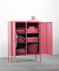 Pink storage cabinet with folded blankets and a cup on a white background