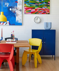 Colorful dining area with red and yellow chairs, a blue cabinet, and abstract art on the wall.