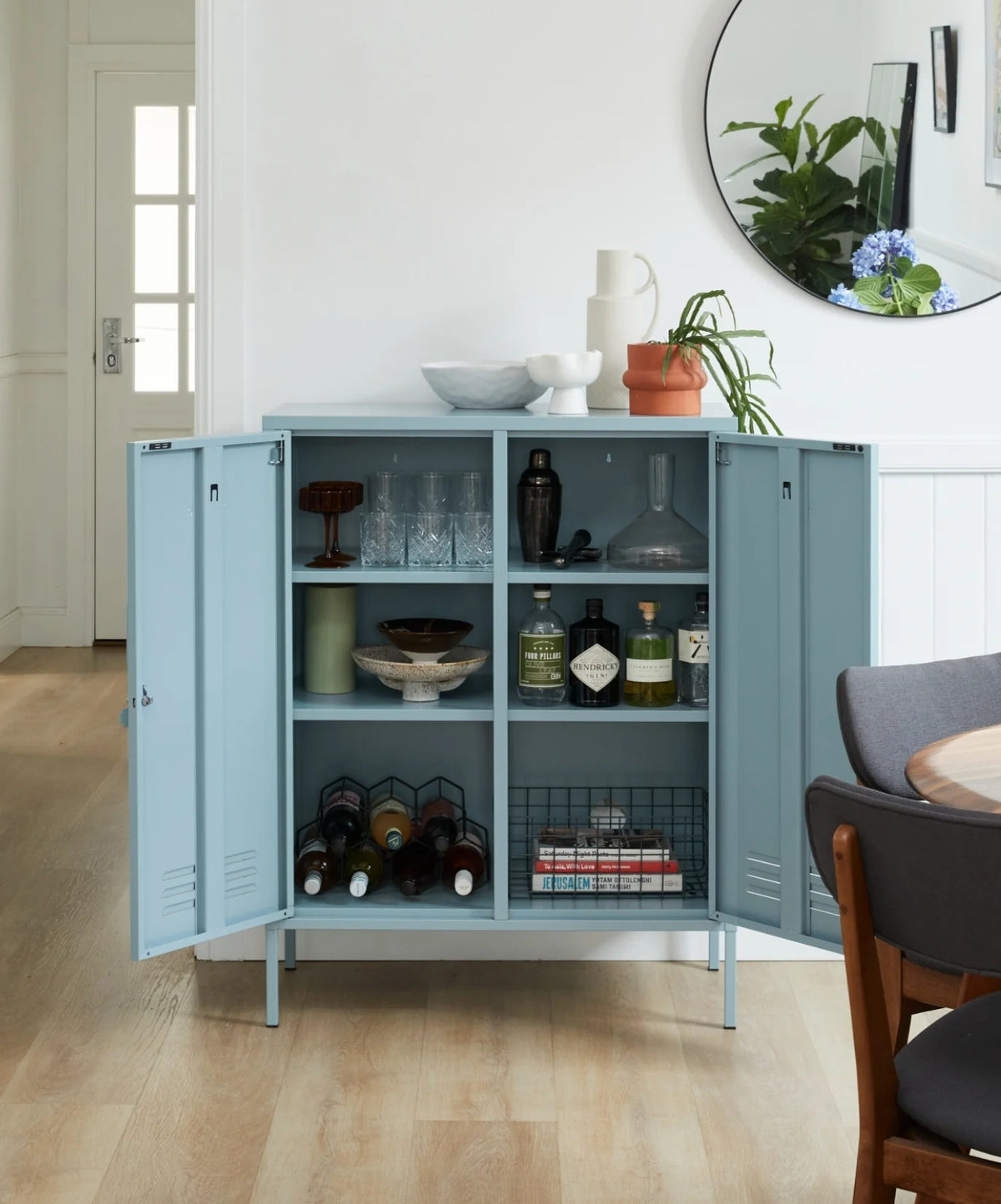 Light blue storage cabinet with open doors displaying bottles and decor items in a room.