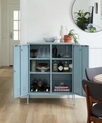 Light blue storage cabinet with open doors displaying bottles and decor items in a room.