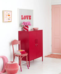 Red cabinet with a chair and decorative items in a room with a pink door.