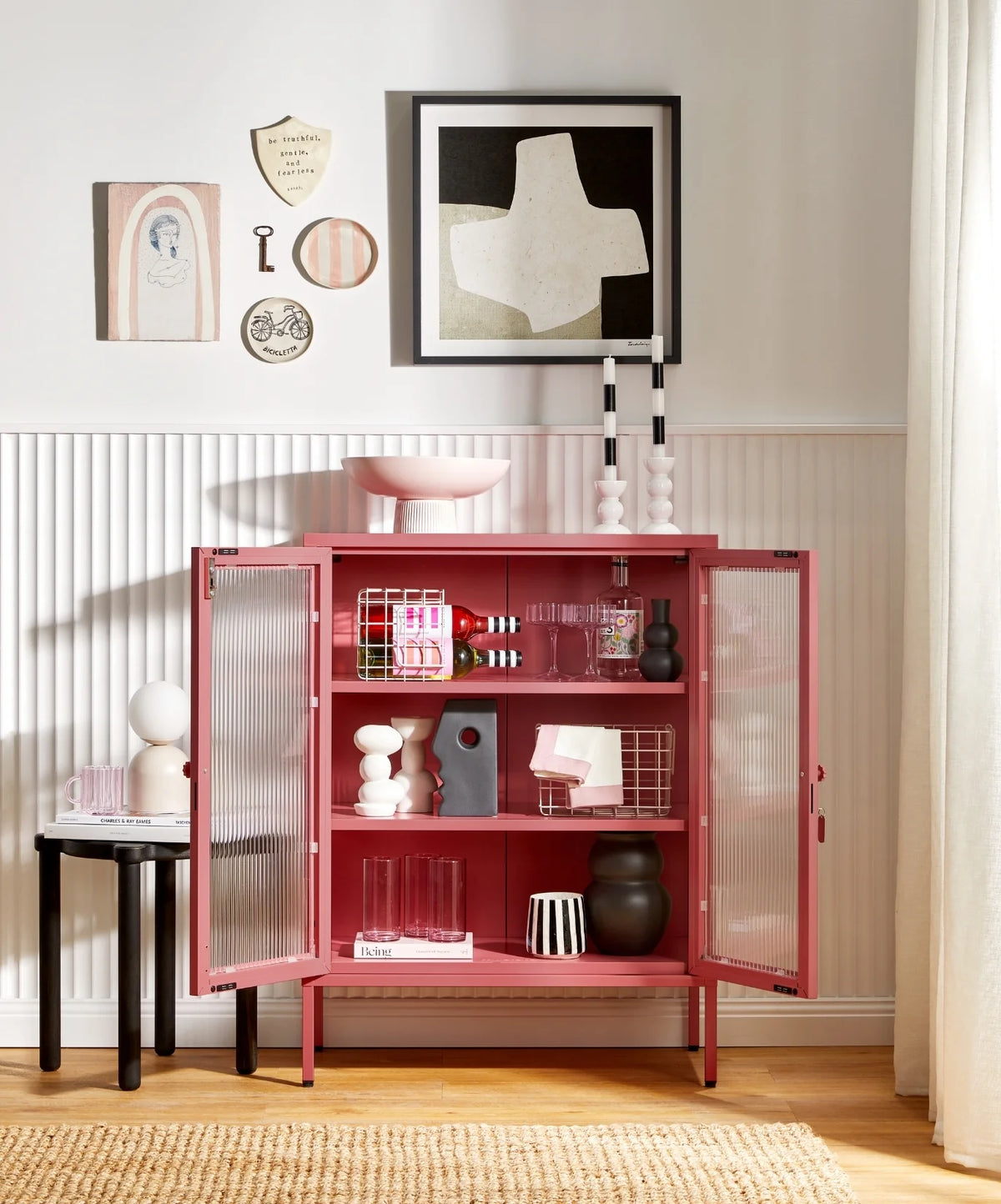 Pink storage cabinet with open doors in a room with decor elements.