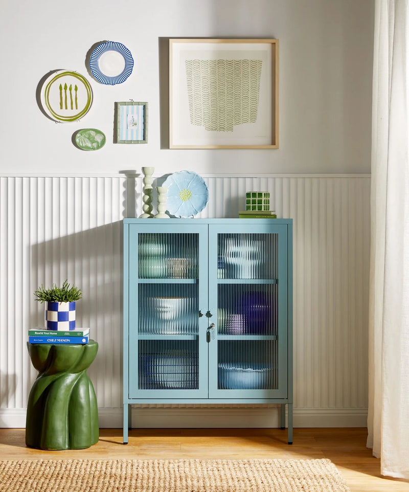 Light blue glass-front cabinet in a room with decorative items and wall art.