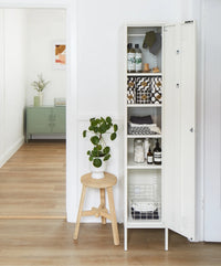White locker cabinet with open door displaying various items, including a plant on a wooden stool.