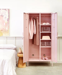 Pink locker in a room with clothes hung inside next to a bed and wall art 