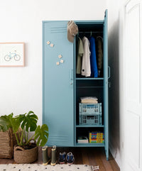 Blue locker with clothes and storage boxes in a room with plants and a bicycle picture.