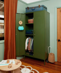 Green metal wardrobe with clothes and items in a room with wooden floor and light blue walls.