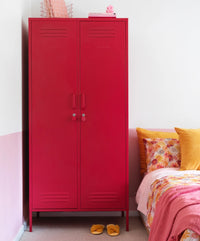 Red metal cabinet in a bedroom with a bed and colorful pillows.