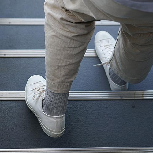 Person wearing beige pants, grey socks and white sneakers stepping onto blue stairs with metal strips.