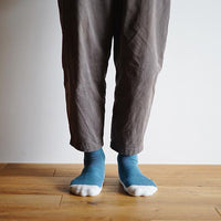 person standing on a wooden floor wearing teal and white socks and brown pants