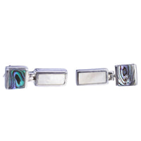 Pair of silver earrings on their sides with abalone shell design on a white background