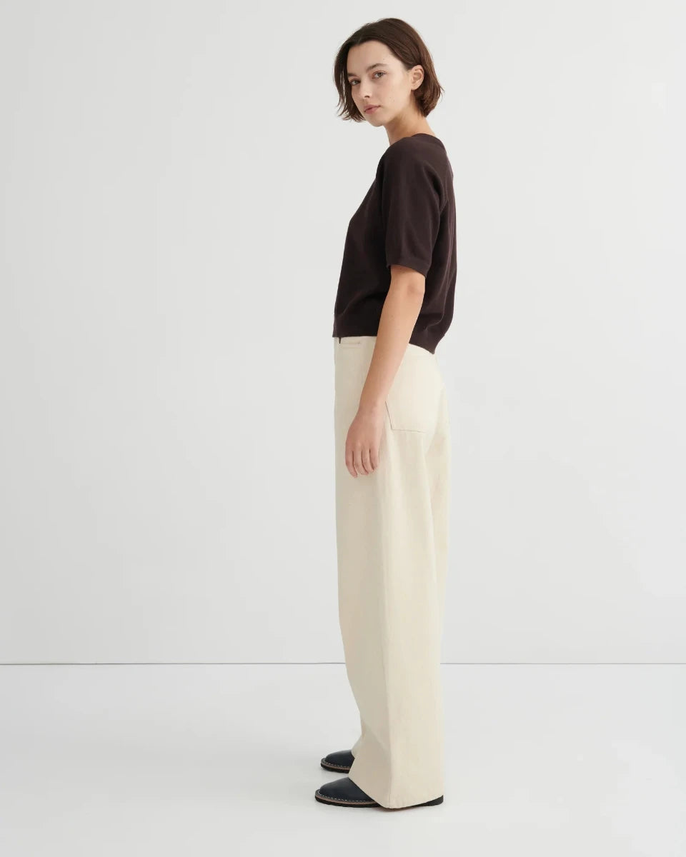 Woman wearing a dark brown short sleeve knit tee and beige pants on a white background