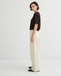 Woman wearing a dark brown short sleeve knit tee and beige pants on a white background