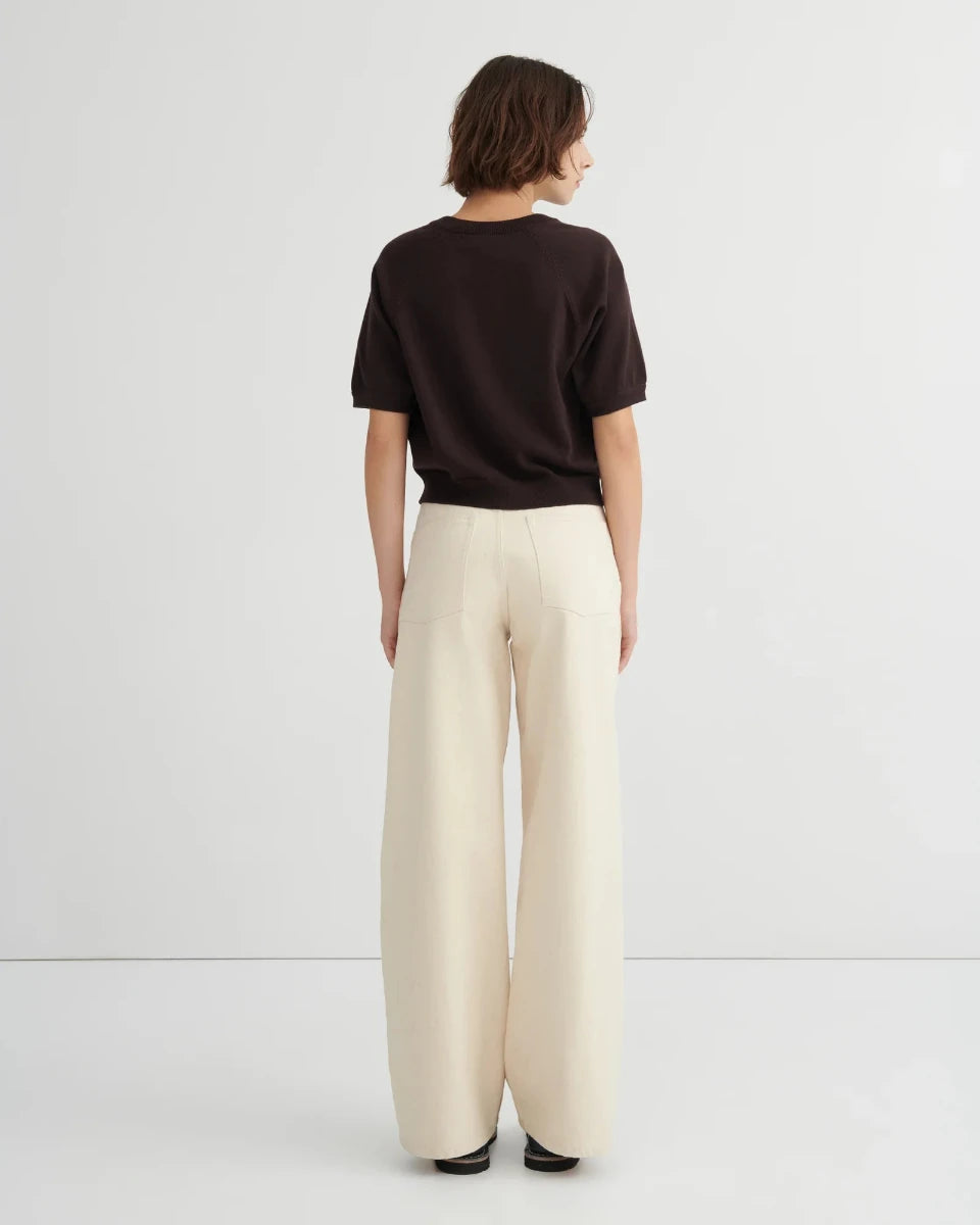Woman wearing a dark brown short sleeve knit tee and beige pants on a white background