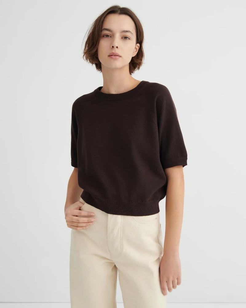 Woman wearing a dark brown short sleeve knit tee and beige pants on a white background