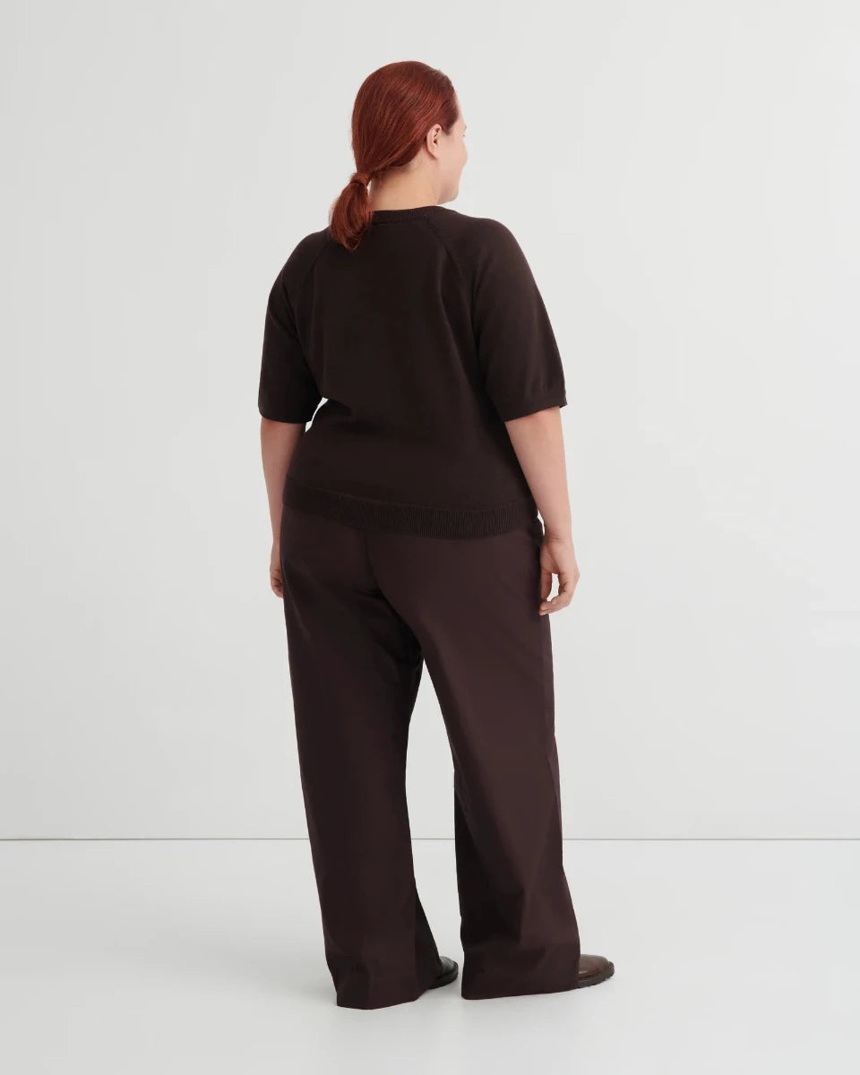 Backside of woman wearing a dark brown short sleeve knit tee and brown pants on a white background