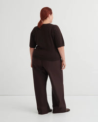 Backside of woman wearing a dark brown short sleeve knit tee and brown pants on a white background