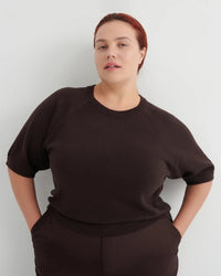 Woman wearing a dark brown short sleeve knit tee and brown pants on a white background